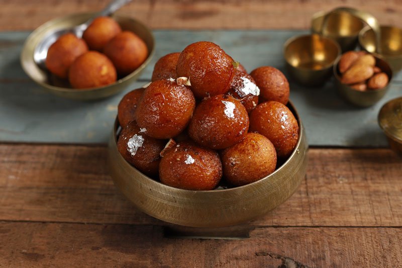 side shot of gulab jamuns stacked in a brass serving bowl