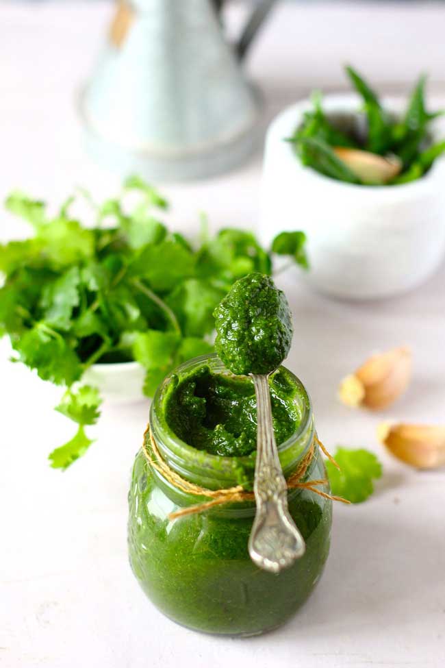 Mint Chutney in a glass bottle with a spoonful of chutney on top.