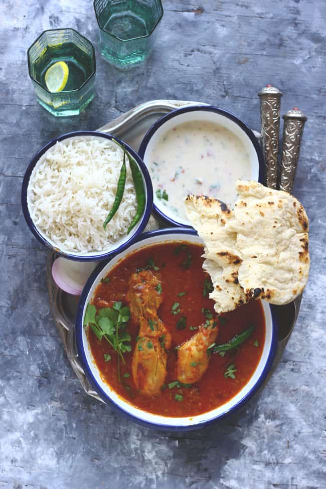 aerial shot of chicken curry with basmati rice, naan. and raita on a plate