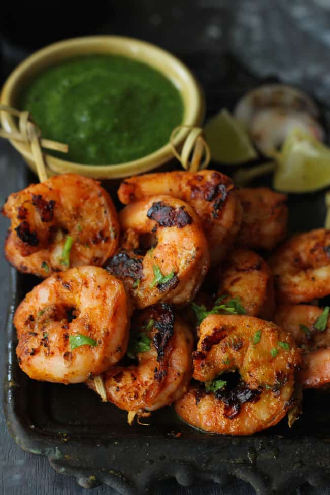 Tandoori Prawn Skewers on a black tray with green chutney.