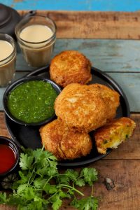side shot of potato bread roll stacked on a black ceramic plate with green chutney