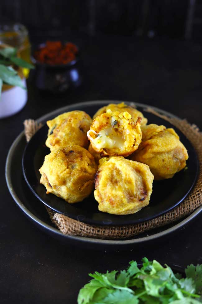 Side shot of aloo bonda on a black plate.