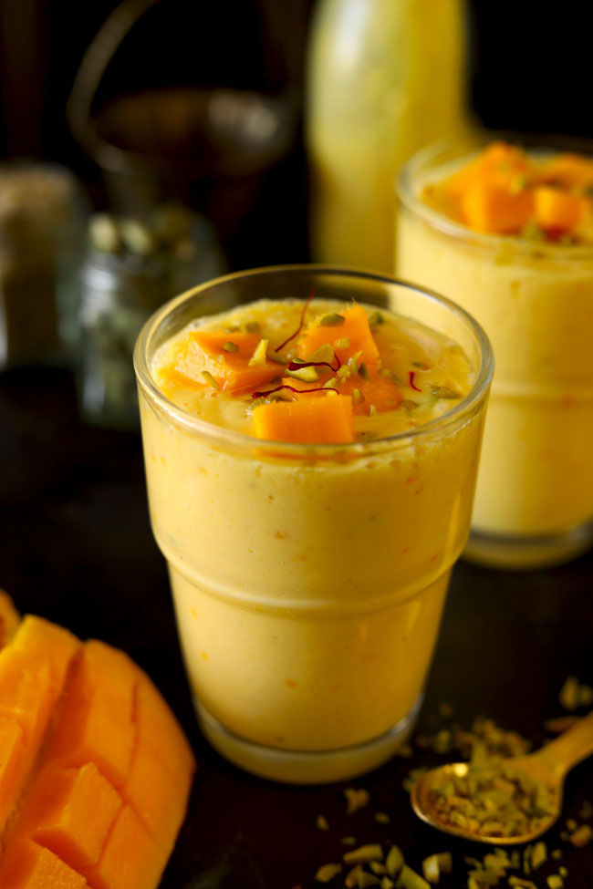 side close up shot of mango lassi in a glass garnished with chopped mango, saffron, and pistachio.