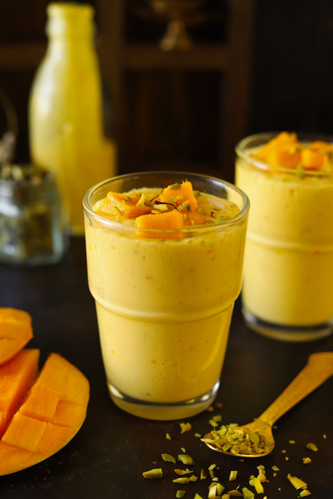 side close up shot of mango lassi in a glass garnished with chopped mango, saffron, and pistachio.