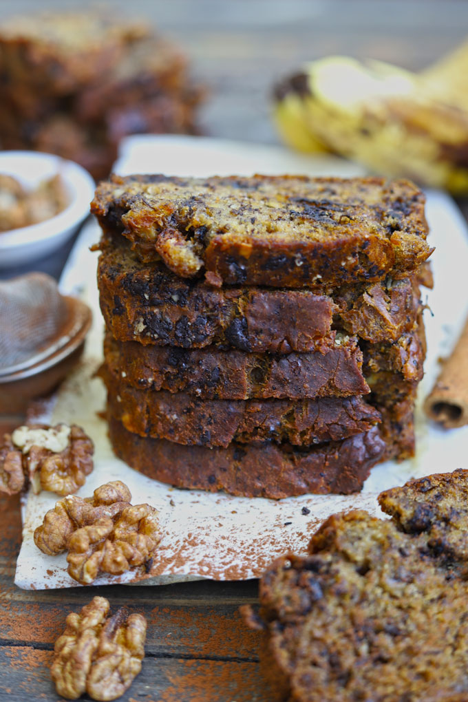 Stack of eggless banana bread slices on a white wooden platter.