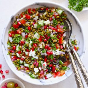Lentil Salad in a white bowl with serving spoons on a white table