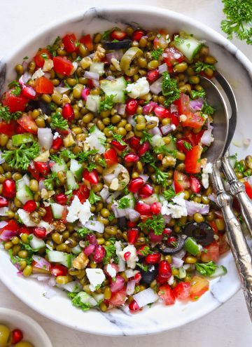 Lentil Salad in a white bowl with serving spoons on a white table