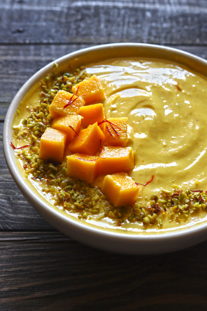 Close Up Shot Of Mango Shrikhand Garnished With Chopped Mango, Pistachio, Saffron In A White Bowl