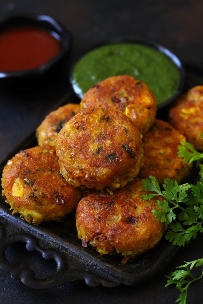 Corn Paneer Cutlet in a Black Tray With Green Chutney Blur In The Background