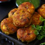 Corn Paneer Cutlet in a Black Tray With Green Chutney Blur In The Background