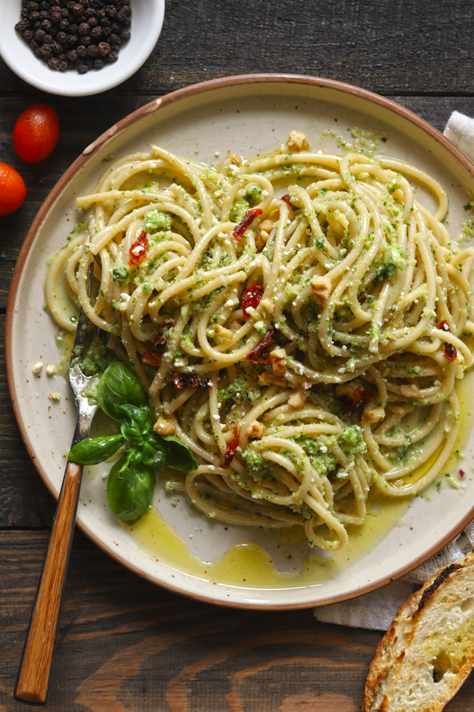 Aerial view of broccoli pesto pasta on wooden table with bread and tomatoes