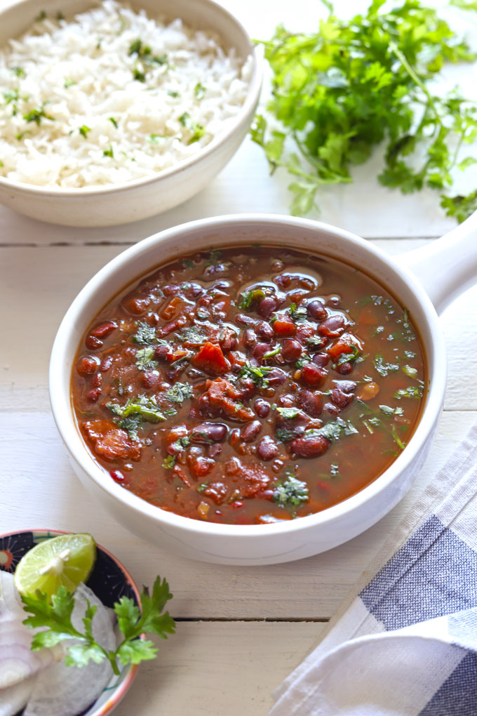 Side shot of rajma curry in a white ceramic serving bowl with steamed rice blur in the background.