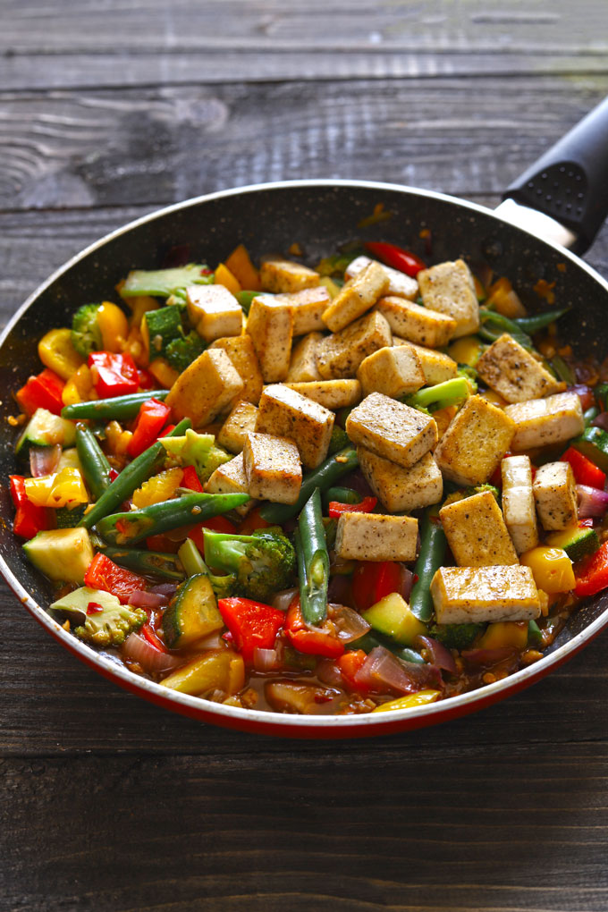 Vegan tofu stir fry in a frying pan on a dark wooden table.