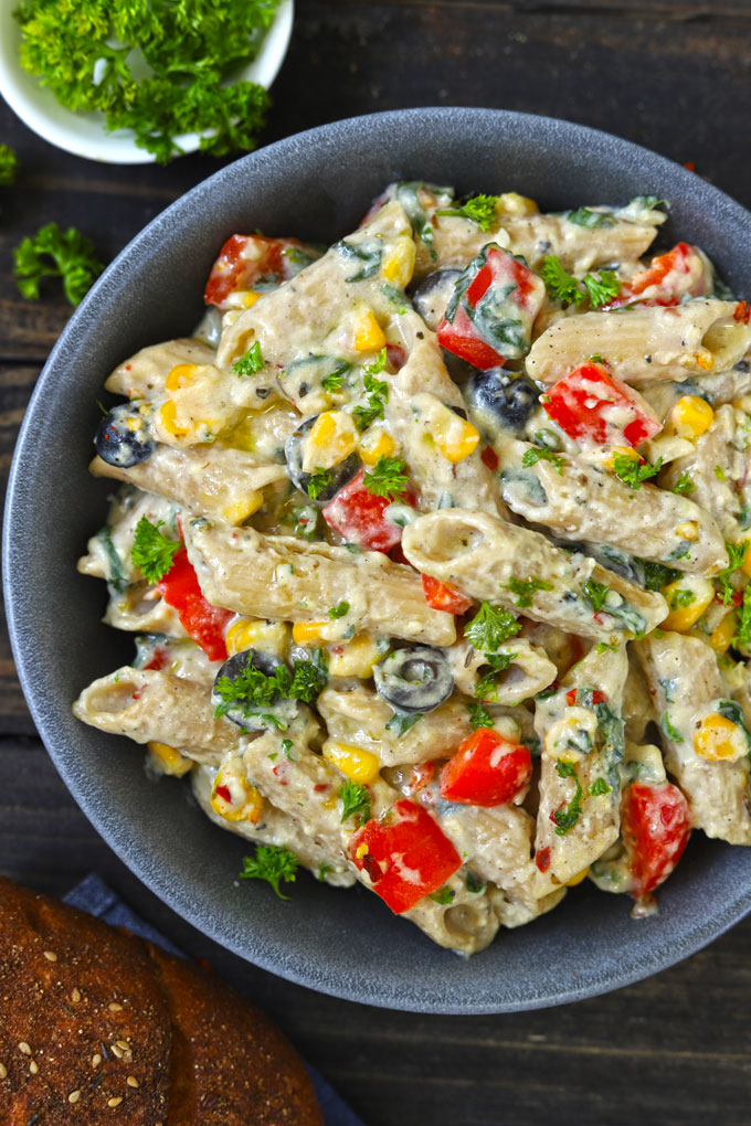 Aerial shot of white sauce penne pasta with veggies in a black bowl.