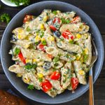 Aerial shot of white sauce penne pasta with veggies in a black bowl.