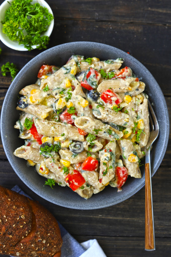 Aerial shot of white sauce penne pasta with veggies in a black bowl.