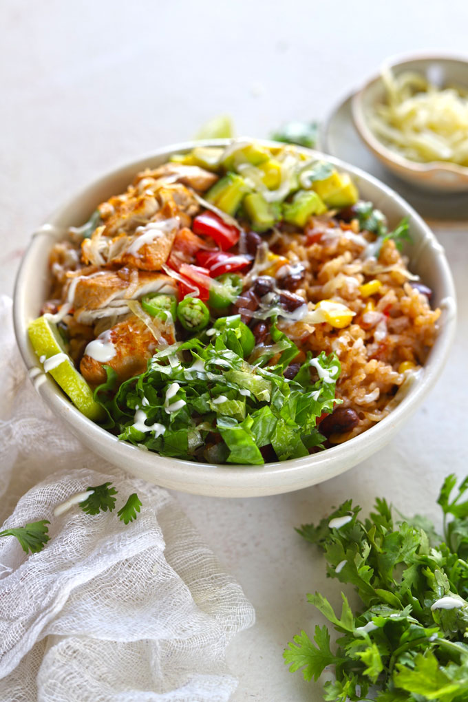 side angle shot of chicken burrito bowl on white table with garnishes and cloth