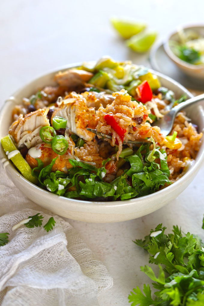 deconstructed burrito in white bowl on white table with garnishes and cloth. Fork is lifting food.