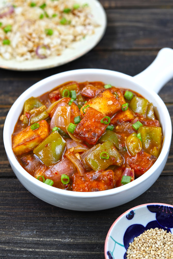 Paneer Chilli in a white serving bowl with fried rice blur in the background.