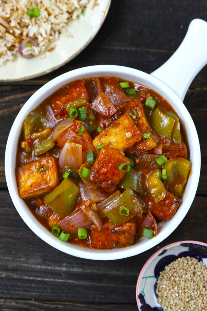 Aerial shot of chilli paneer in a white ceramic serving bowl on a black background.