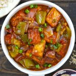 Aerial shot of chilli paneer in a white ceramic serving bowl on a black background.