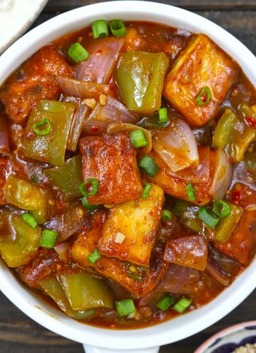 Aerial shot of chilli paneer in a white ceramic serving bowl on a black background.