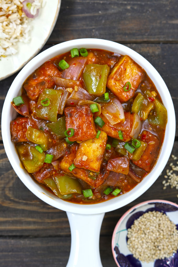 Aerial shot of chilli paneer in a white ceramic serving bowl on a black background.