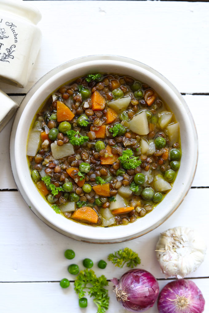 Aerial shot of lentil stew in a white ceramic serving bowl on a white background.