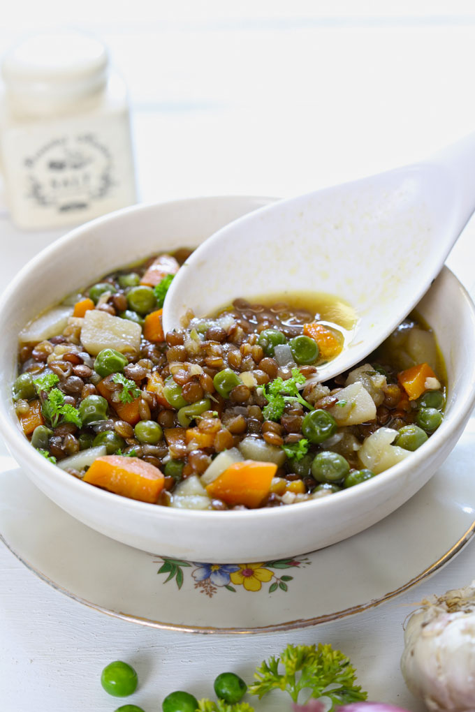 Lentil Stew in a white ceramic serving bowl with a serving spoon on a white background.