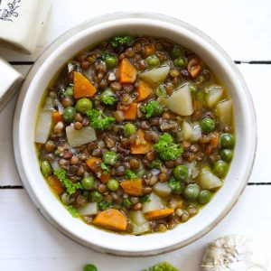 Aerial shot of lentil stew in a white ceramic serving bowl on a white background.