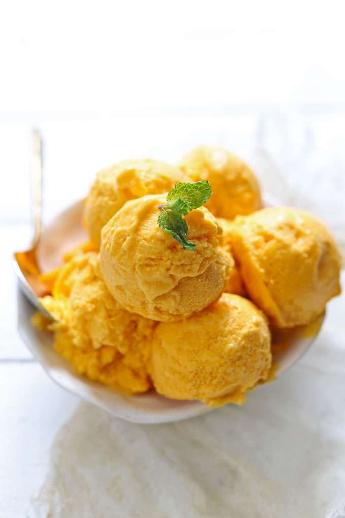 Side shot of mango ice cream scoops in a white serving bowl.