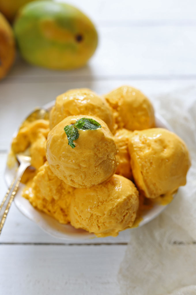 Side shot of mango ice cream scoops in a white serving bowl.