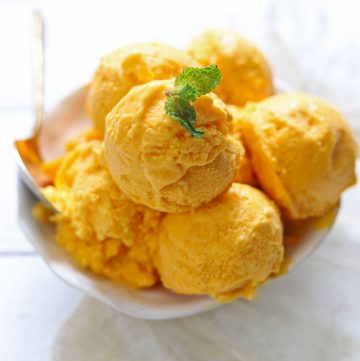 Side shot of mango ice cream scoops in a white serving bowl.