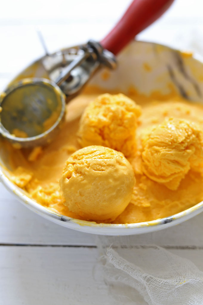 Side shot of mango ice cream scoops in a white bowl with a scooper