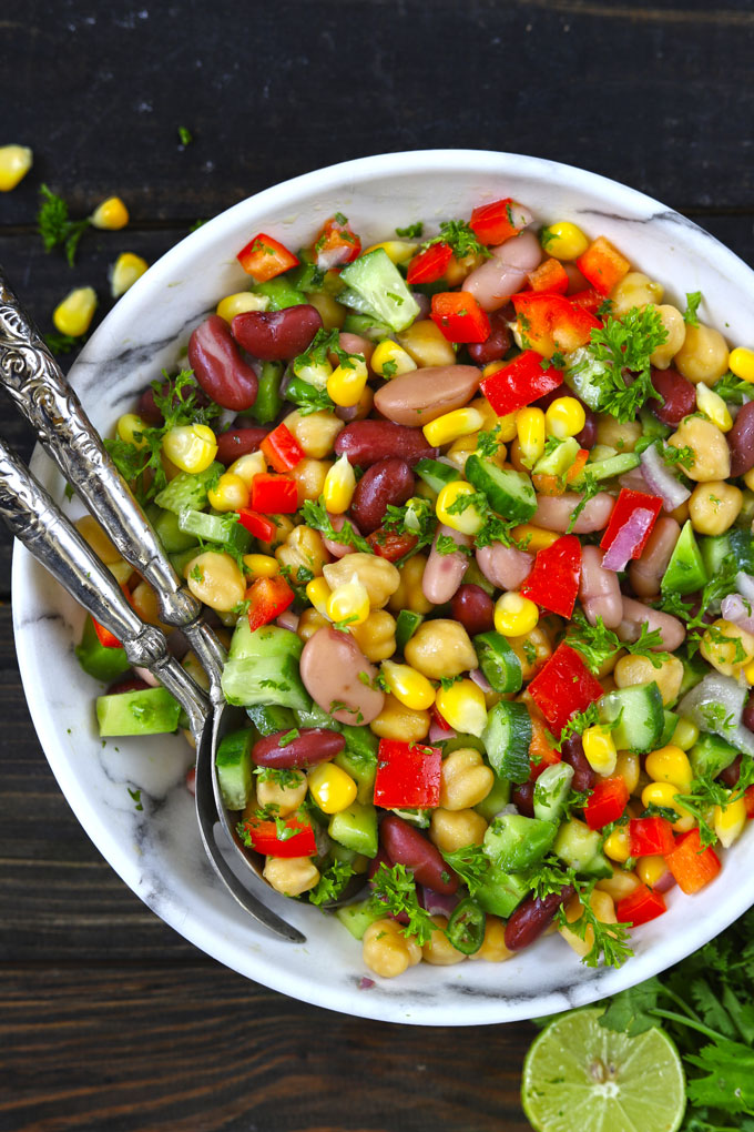 Aerial shot of Mexican style mixed beans salad in a white bowl with silver serving bowls. 