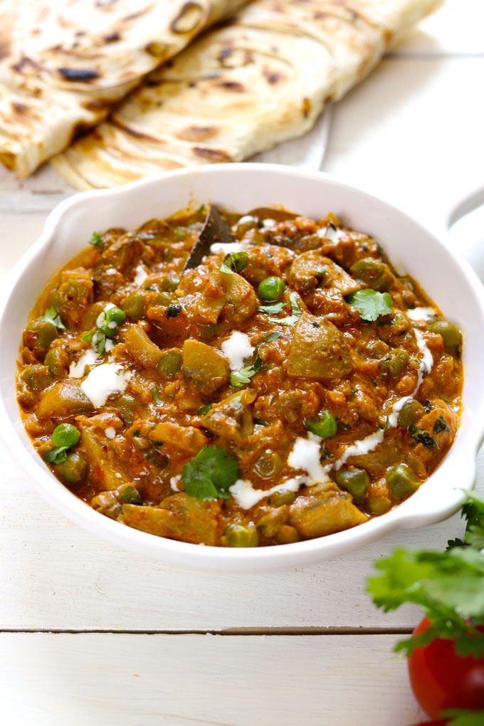 Side shot of Indian matar mushroom curry in a white pan with paratha blur in the background.