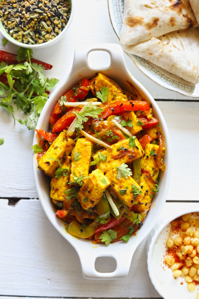 Aerial shot of paneer jalfrezi in an oval, white ceramic serving dish with roti on the side.