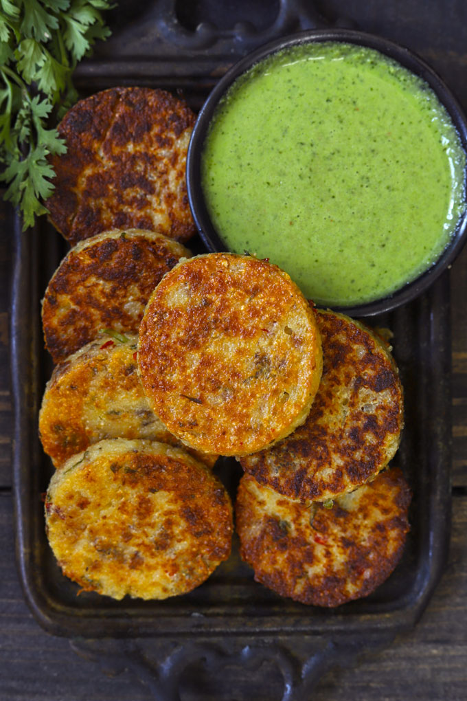 Aerial shot of suji cutlet in a black tray with green chutney on the side.