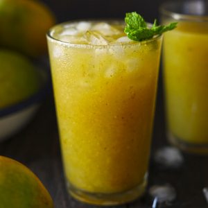 Side shot of yellow color aam panna in a glass garnished with mint leaves.