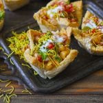 Side shot of bread basket chaat on a black tray.