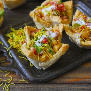 Side shot of bread basket chaat on a black tray.