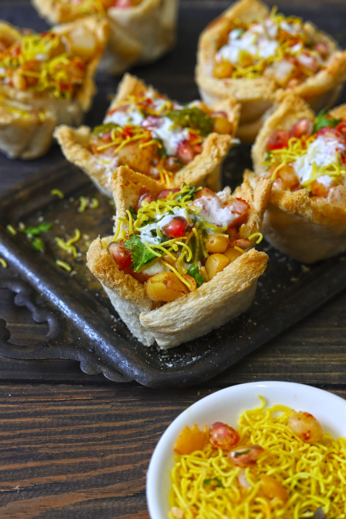 Side shot of bread basket chaat on a black tray.