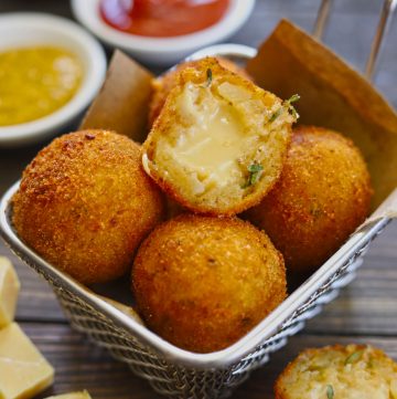 Side shot of stacked potato cheese balls in a frying basket.