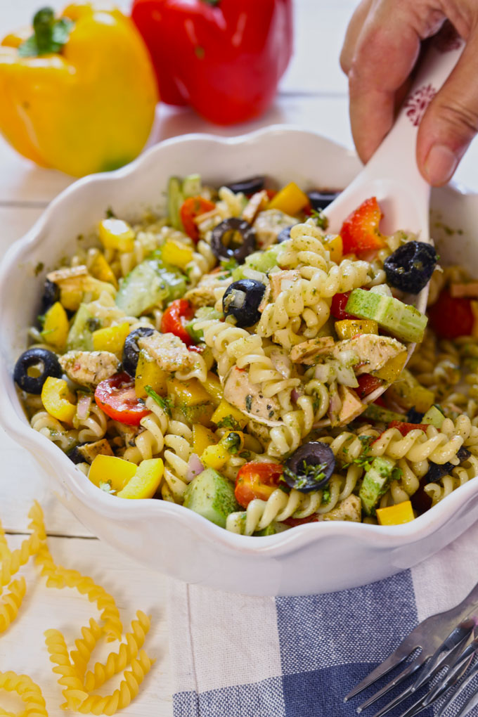 Side shot of mixing pasta salad in a white ceramic serving bowl