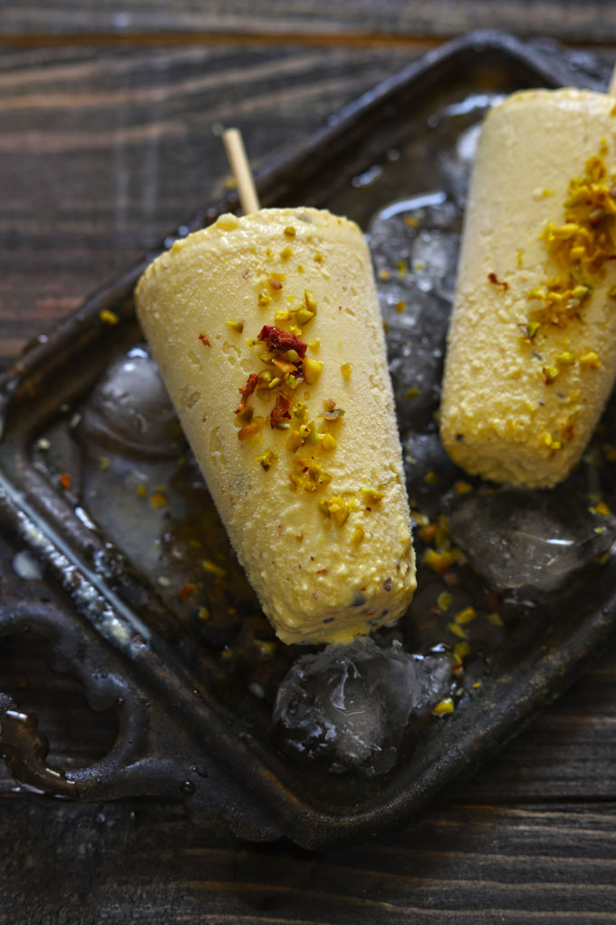 Aerial shot of two kesar pista kulfi on a black tray filled with crushed ice.