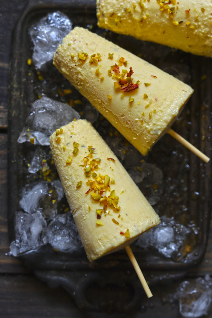 Aerial shot of two kesar pista kulfi on a black tray filled with crushed ice.