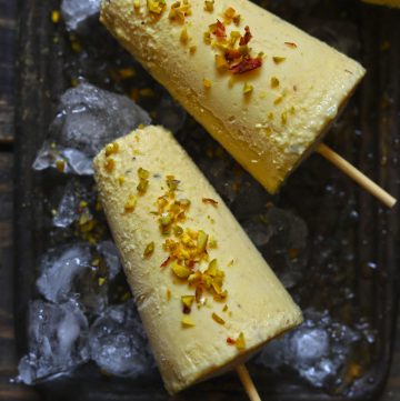 Aerial shot of two kesar pista kulfi on a black tray filled with crushed ice.