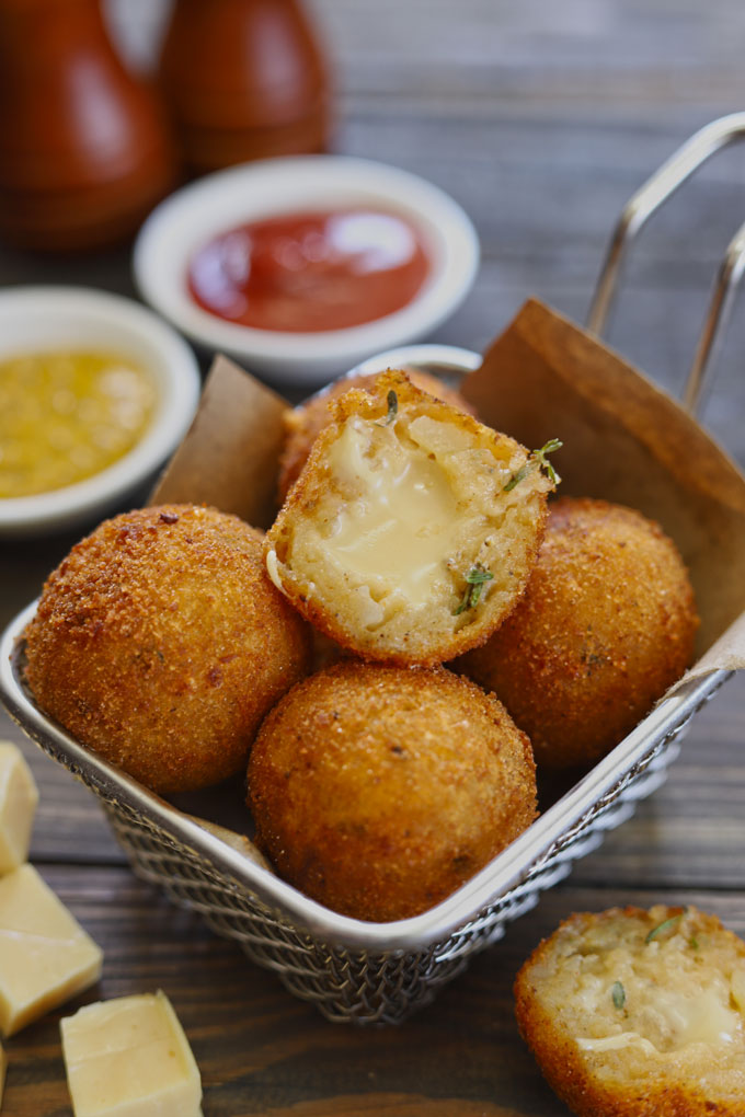 Side shot of stacked potato cheese balls in a frying basket.