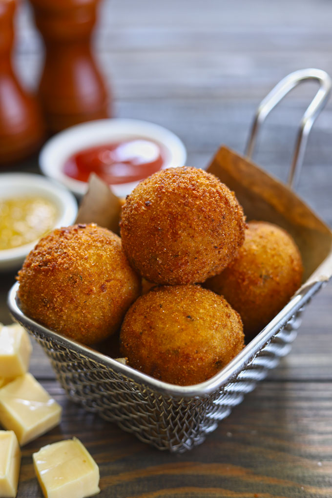 Side shot of stacked potato cheese balls in a frying basket.