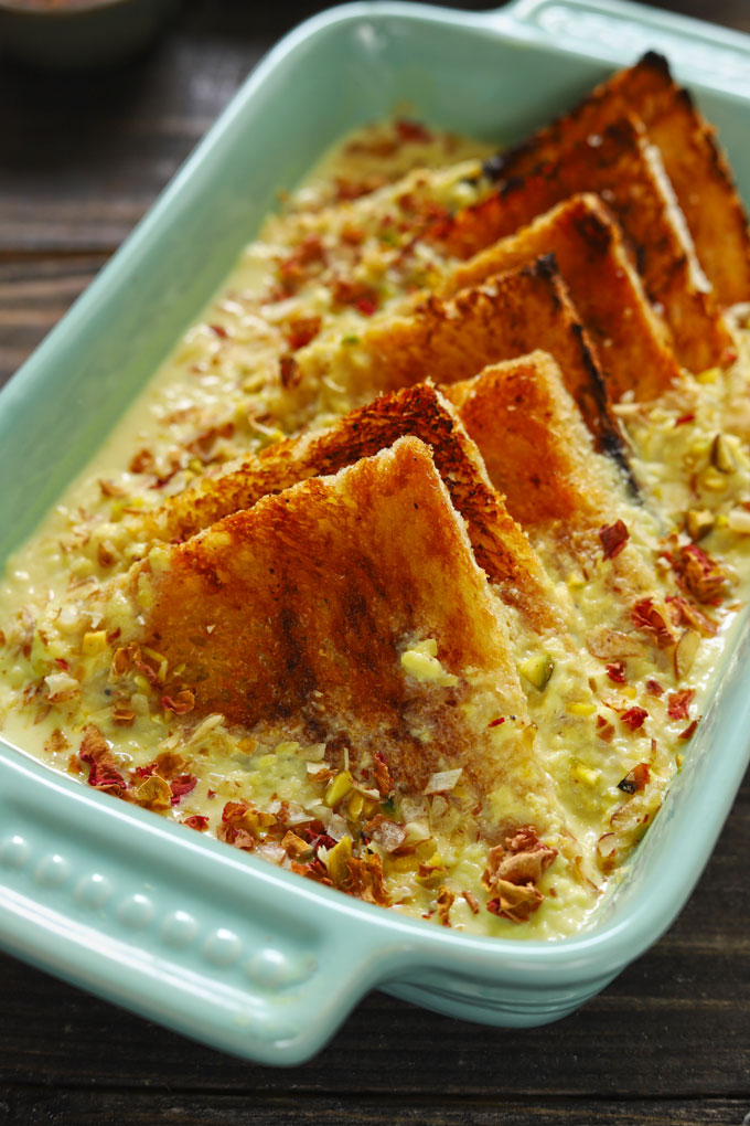 Side shot of baked shahi tukda in a green ceramic baking dish.